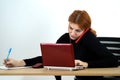 Young office worker woman talking on a cell phone sitting behind working desk with laptop computer and notebook Royalty Free Stock Photo