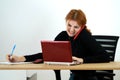 Young office worker woman talking on a cell phone sitting behind working desk with laptop computer and notebook Royalty Free Stock Photo