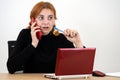 Young office worker woman talking on a cell phone sitting behind working desk with laptop computer and notebook Royalty Free Stock Photo