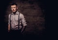 Young old-fashioned tattooed guy wearing white shirt and suspenders, looking at a camera on a dark background. Royalty Free Stock Photo