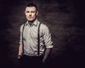 Young old-fashioned tattooed guy wearing white shirt and suspenders, looking at a camera on a dark background. Royalty Free Stock Photo