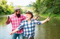 Young and old fisherman standing on the shore of lake with fishing rod. Father and son enjoy life. Men family, granddad Royalty Free Stock Photo