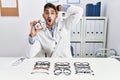 Young optician man holding optometry glasses crazy and scared with hands on head, afraid and surprised of shock with open mouth Royalty Free Stock Photo