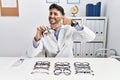 Young optician man holding optometry glasses pointing with hand finger to face and nose, smiling cheerful Royalty Free Stock Photo