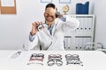 Young optician man holding optometry glasses smiling and laughing with hand on face covering eyes for surprise Royalty Free Stock Photo
