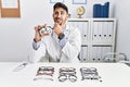 Young optician man holding optometry glasses thinking worried about a question, concerned and nervous with hand on chin Royalty Free Stock Photo