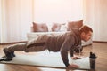 Young ordinary man go in for sport at home. Beginner freshman in exercising guy stand in plank position and look forward