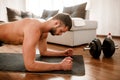 Young man go in for sport at home. Cut view of t-shirtless guy sportsman with a sports figure stand in plank position