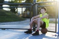 young outdoors sitting on basket ball at a street court with ball