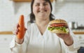 Young overweight plus size fat woman holding a burger in one hand and a carrot in other. Royalty Free Stock Photo