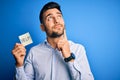 Young overworked business man asking for help holding paper over blue background serious face thinking about question, very Royalty Free Stock Photo