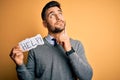 Young overworked business man asking for help holding paper over yellow background serious face thinking about question, very Royalty Free Stock Photo