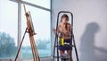 Young painter is drawing picture in art studio, standing near big windows.