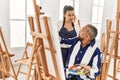Young painting teacher woman teaching art to senior man painting on canvas at art studio