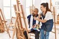 Young painting teacher woman teaching art to senior man painting on canvas at art studio