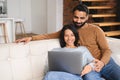 Young Pakistani couple using laptop while sitting on the sofa at home. Spouses watching movie on laptop. Happy man and Royalty Free Stock Photo