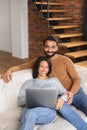 Pakistani couple using laptop while sitting on the sofa at home. Spouses watching movie on laptop. Happy man and woman Royalty Free Stock Photo