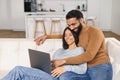 Young Pakistani man pointing at the screen while using laptop on the sofa at home with his wife. Spouses watching Royalty Free Stock Photo