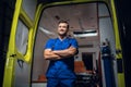 Young paramedic in a blue uniform standing and smiling in front of an an ambulance car Royalty Free Stock Photo