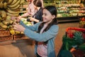 Young parents and daughter in grocery store. Child touch yellow bananas and smile. She is happy. Man and woman stand Royalty Free Stock Photo