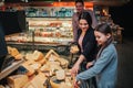 Young parents and daughter in grocery store. Mother help daughter to pick up cheese. Father stand behind and look at it