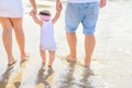 Young Parents Holding by Hands Cute Little Baby Toddler Girl Daughter Learning to Walk. Beach Sea Sunlight. Authentic Royalty Free Stock Photo