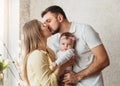 Young parents kiss each other and hold a baby girl in their arms. Parenthood