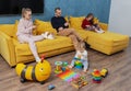 Young parents are sitting on a cozy sofa in the apartment, a little kid is playing on the floor with toys. Royalty Free Stock Photo