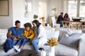 Young parents sitting on sofa with their daughter using tablet computer in open plan living room, grandparents sitting at a table 