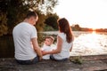 Young parents and their little son sitting on the wooden pier near the lake, at sunset on summer day Royalty Free Stock Photo