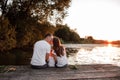 Young parents and their little son sitting on the wooden pier near the lake, at sunset on summer day Royalty Free Stock Photo