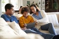 Young parents and their pre-teen daughter sitting on a sofa in the living room using a tablet computer together, selective focus Royalty Free Stock Photo