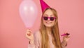 Young party woman blowing party horn whie holding balloon. Isolated on pink background Royalty Free Stock Photo