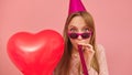Young party woman blowing party horn whie holding heart shaped balloon. Isolated on pink background Royalty Free Stock Photo