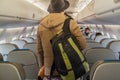 Handsome young passenger in a warm jacket and hat stands with a backpack in the cabin of airplane.