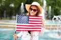 Young patriot woman in hat smilig and stretching USA flag in park