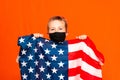 Young patriotic 9s child wears face mask holding united states of america flag on orange studio shot