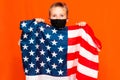 Young patriotic 9s child wears face mask holding united states of america flag on orange studio shot