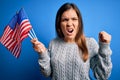 Young patriotic woman holding usa flag on independence day 4th of july over blue background annoyed and frustrated shouting with