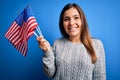 Young patriotic woman holding usa flag on independence day 4th of july over blue background with a happy face standing and smiling