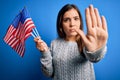 Young patriotic woman holding usa flag on independence day 4th of july over blue background with open hand doing stop sign with