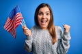 Young patriotic woman holding usa flag on independence day 4th of july over blue background screaming proud and celebrating