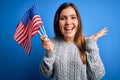 Young patriotic woman holding usa flag on independence day 4th of july over blue background very happy and excited, winner