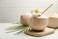 Young peeled coconuts with straw, palm leaf and flower on white wooden table. Space for text Royalty Free Stock Photo