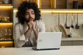 Arabian man works remotely on computer at table in kitchen Royalty Free Stock Photo