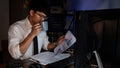 Young pensive asian man working late concentrated and serious in front of computer at night in dark office, Late night working or Royalty Free Stock Photo