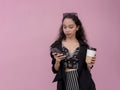 A young pensive asian woman chatting on her phone while holding a cup of coffee. Isolated on a light pink background.