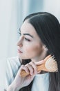 young pensive brunette woman combing hair with hairbrush and looking Royalty Free Stock Photo