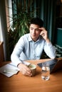 Young pensive business man wearing classic clothes working at modern city cafe with laptop and papers on desk. Freelance Royalty Free Stock Photo