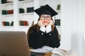 Young pensive caucasian woman college student in graduation outfit , sitting in front laptop with books and thinking about future Royalty Free Stock Photo